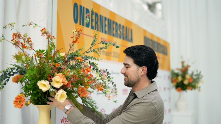 Man adding flowers to a large vase during an event.