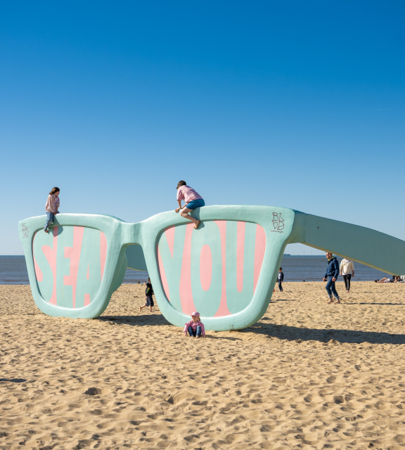 Large art installation of sunglasses reading 'SEA YOU' on Scheveningen beach.