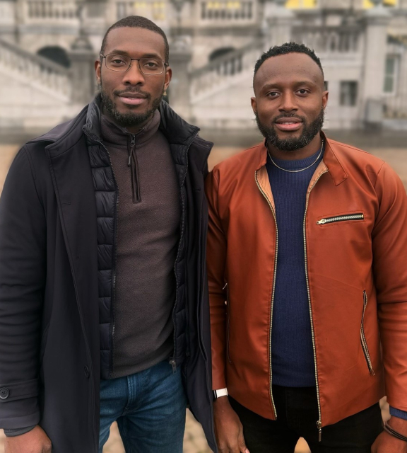 Two men stand next to each other in front of a building.