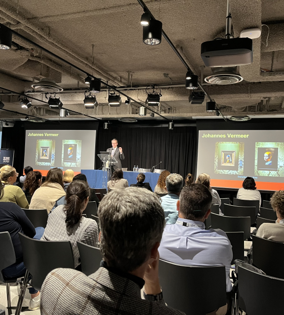 A speaker presents to an audience with images of Vermeer.