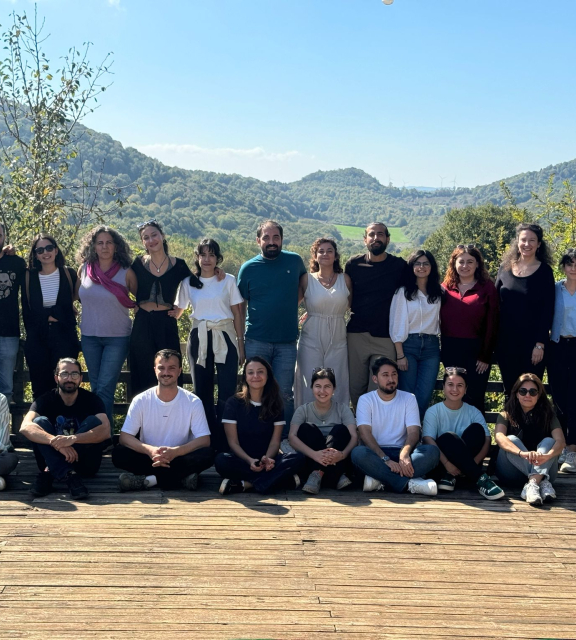 A group of people poses on a wooden deck with green hills in the background.