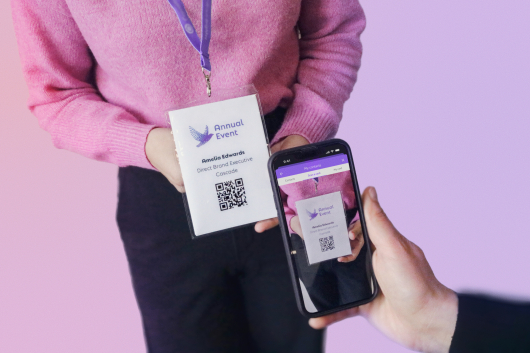 A person holds an event badge while a smartphone scans the QR code.