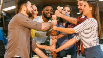 Photo of people teambuilding by creating a tower with their fists. 