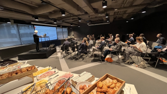 A speaker presents to an audience in a room with snacks.