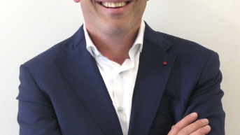A man with a bald head and a blazer smiling warmly.