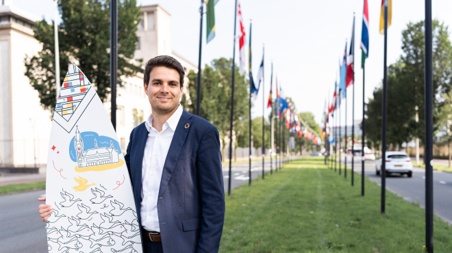 Image of international sales advisor Joris holding branded surfboard of The Hague in the International Zone of The Hague