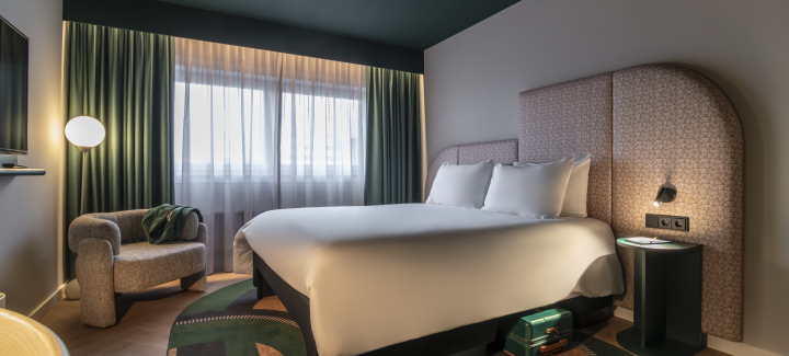A stylish hotel room featuring a bed, an armchair, and windows with curtains.