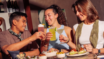 Three people toasting with colorful drinks at a table