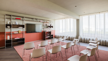 A modern meeting room with a TV, shelving, and chairs.