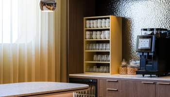 A modern kitchen featuring a bar, glass cabinet, and coffee machine.