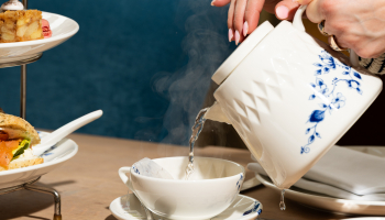 A hand is pouring steaming tea into a cup.