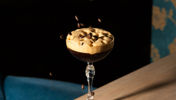 A cocktail glass filled with coffee drink topped with coffee beans.