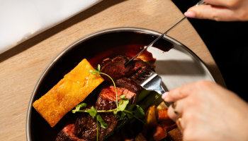 A person is cutting a steak with vegetables and sauce.