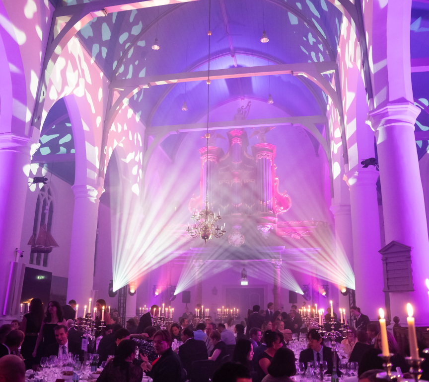 Interior of a hall with a light show and guests at dinner tables.