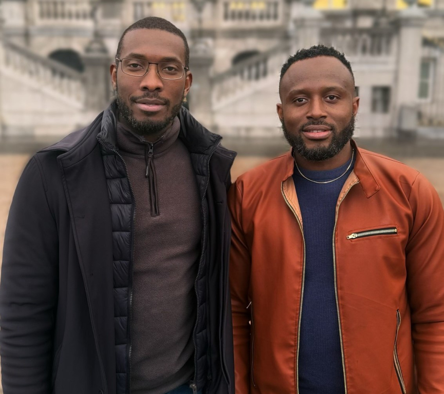 Two men stand next to each other in front of a building.