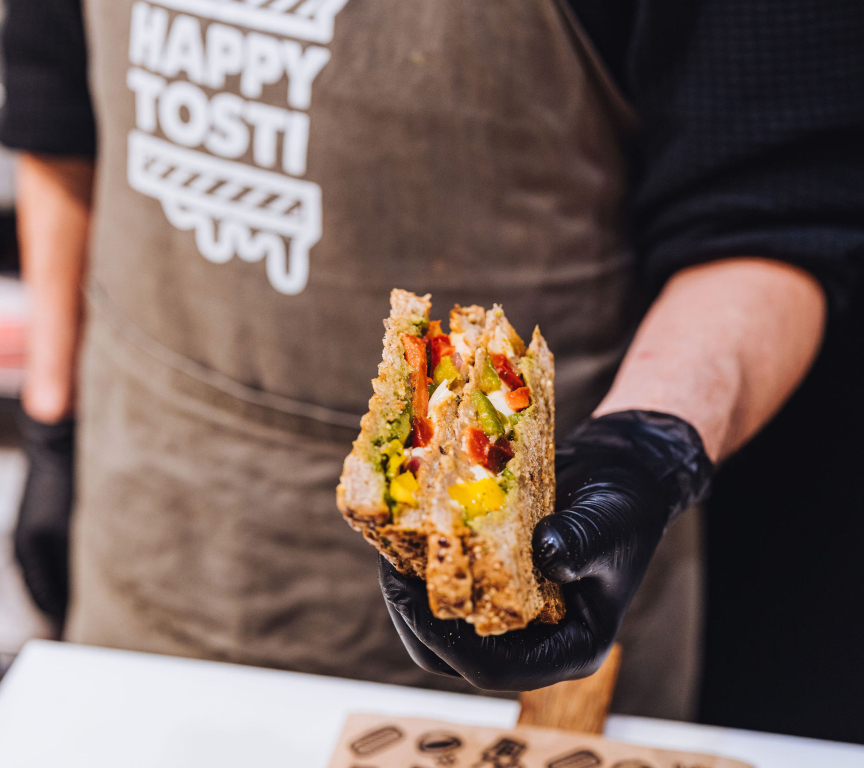 A hand holds a grilled vegetarian toast with vegetables.