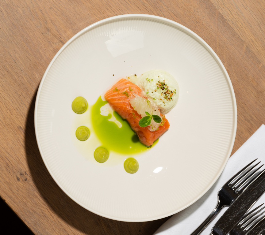 A plate with salmon, white sauce, and green drops.
