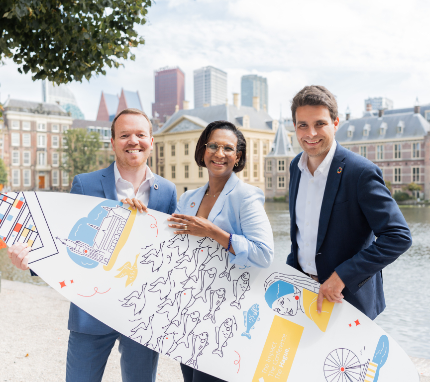 Image of three people of The Hague and Partners holding a branded surfboard standing in front of the Hofvijver in The Hague