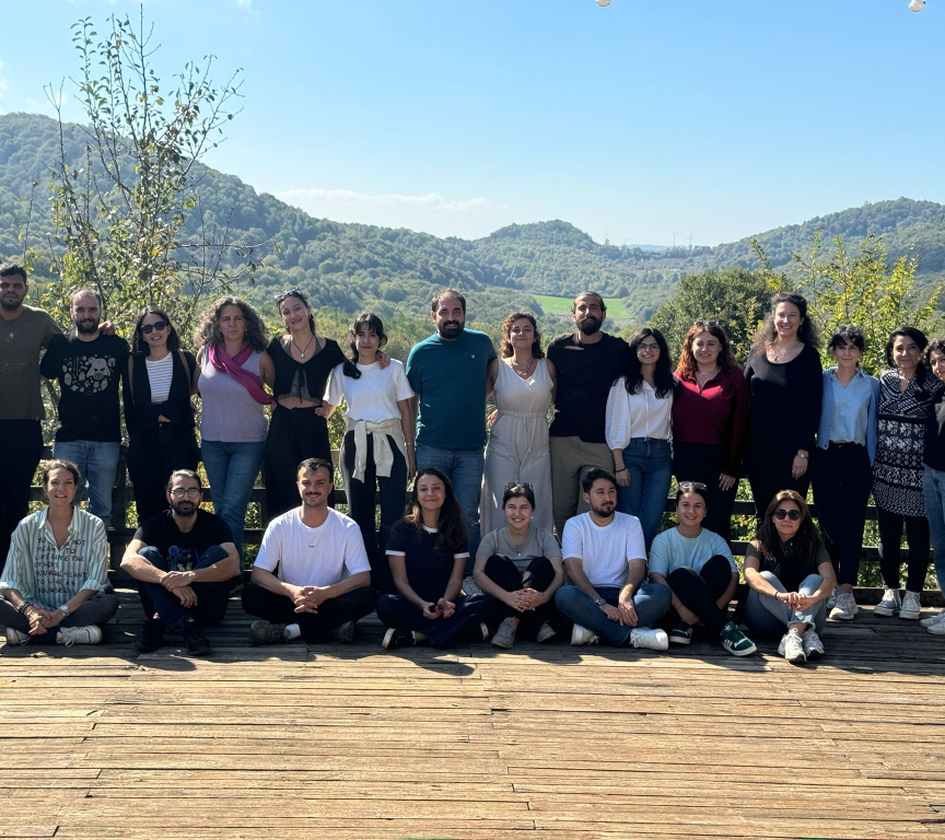 A group of people poses on a wooden deck with green hills in the background.