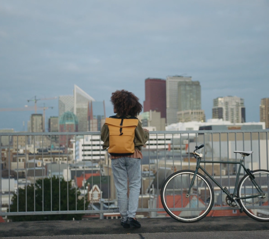 A person with a backpack looking at The Hague skyline with buildings and a bike beside them.