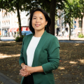 Woman in a green blazer stands in a park.