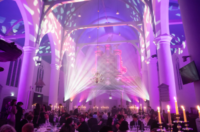 Interior of a hall with a light show and guests at dinner tables.