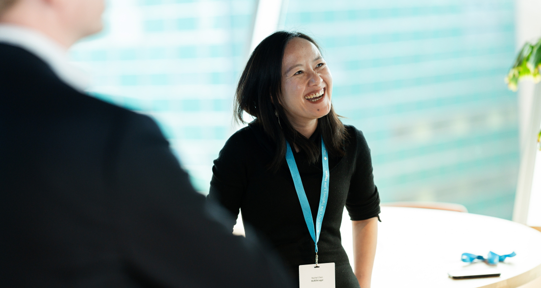 A woman in a black shirt and a blue lanyard smiles while talking to someone.
