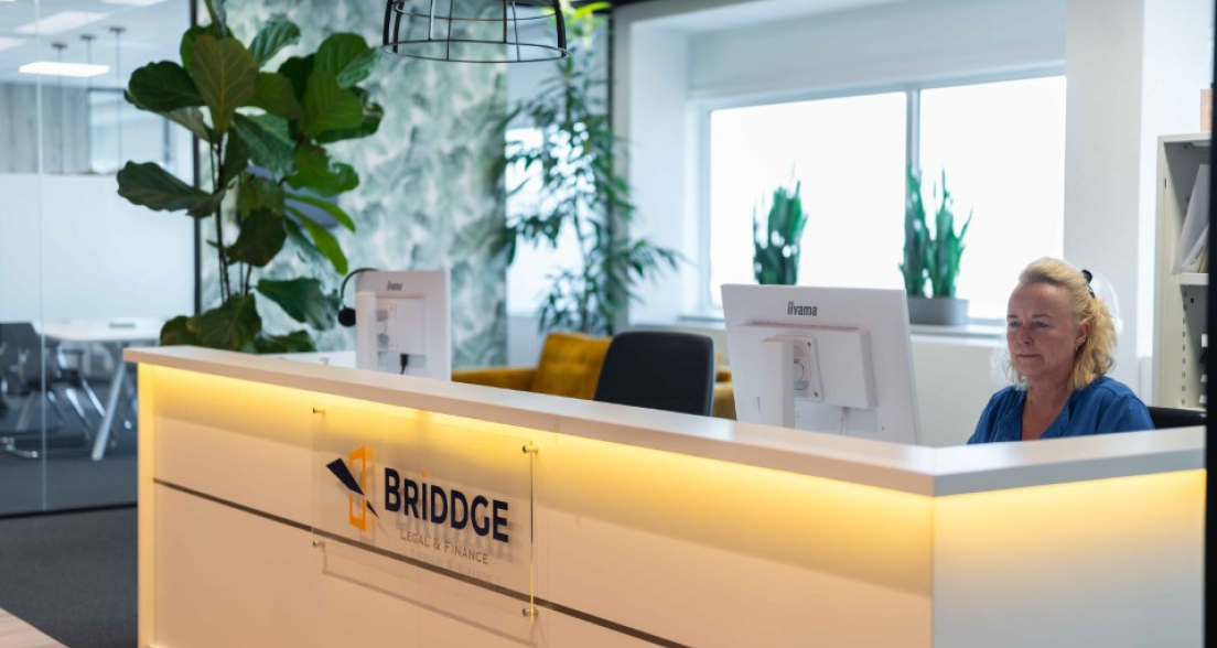 A woman behind the reception desk of Briddge with plants in the background.