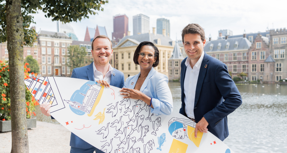 Image of three people of The Hague and Partners holding a branded surfboard standing in front of the Hofvijver in The Hague