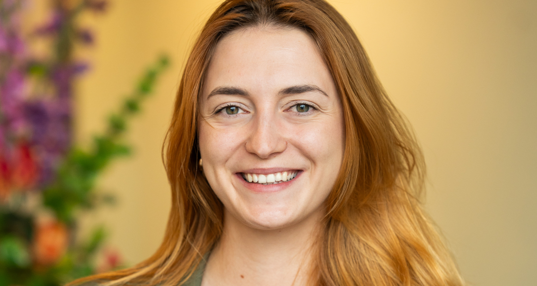 A smiling woman with long, reddish hair and a green vest.