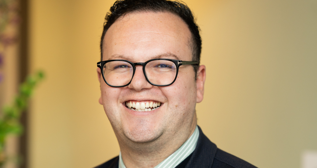 Man with glasses and a smile, wearing a dark blazer.