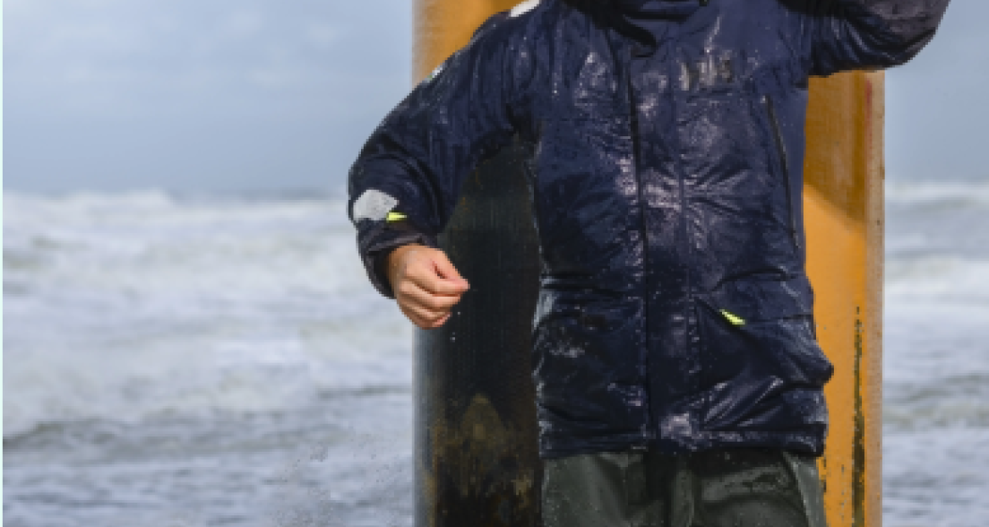 A young man enjoys the sea in rain gear.