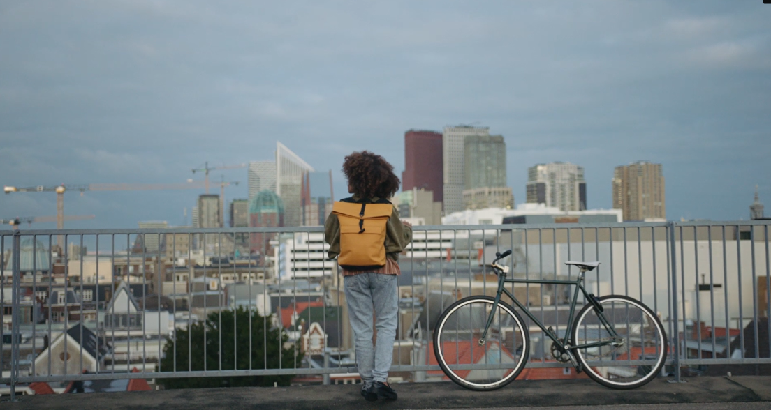 A person with a backpack looking at The Hague skyline with buildings and a bike beside them.