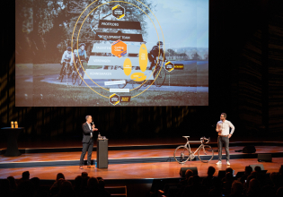 A speaker and a presenter next to a bicycle. Behind them is a presentation about cycling development.