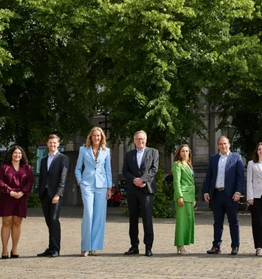 A group of nine people poses in a park filled with trees.