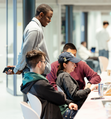 Five students collaborating on a laptop in an open area.