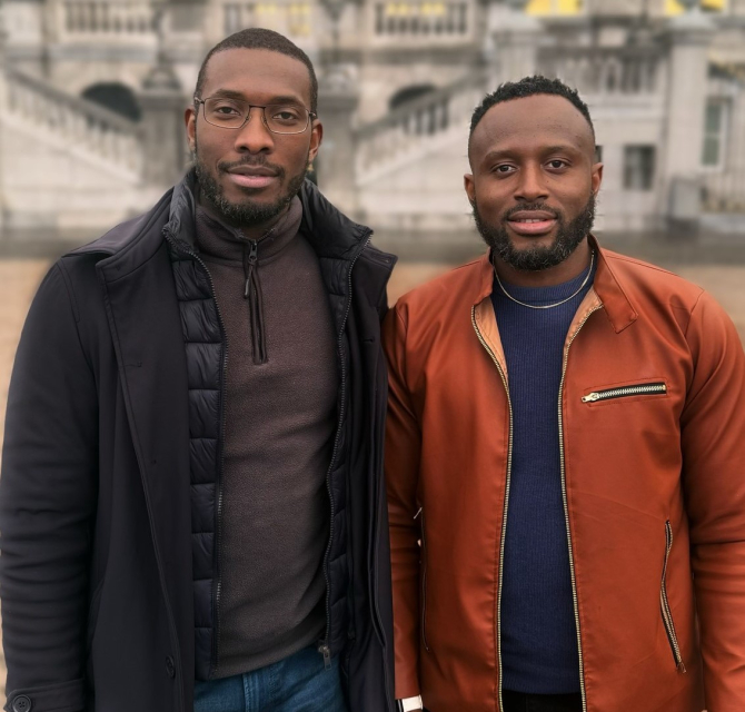 Two men stand next to each other in front of a building.