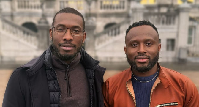 Two men stand next to each other in front of a building.