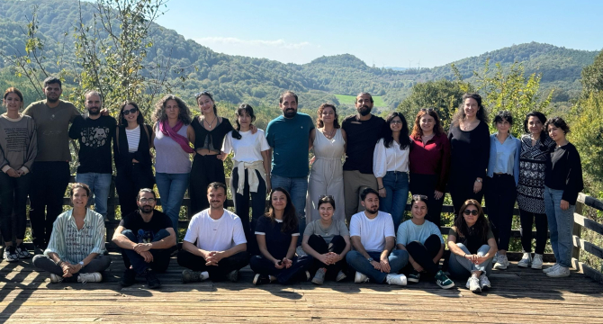 A group of people poses on a wooden deck with green hills in the background.