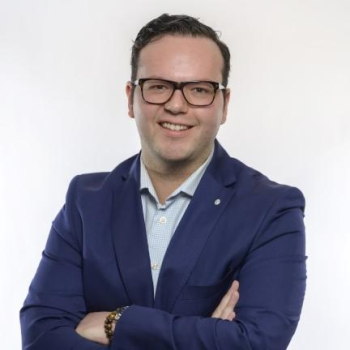 A man in a blazer and glasses, smiling against a white background.