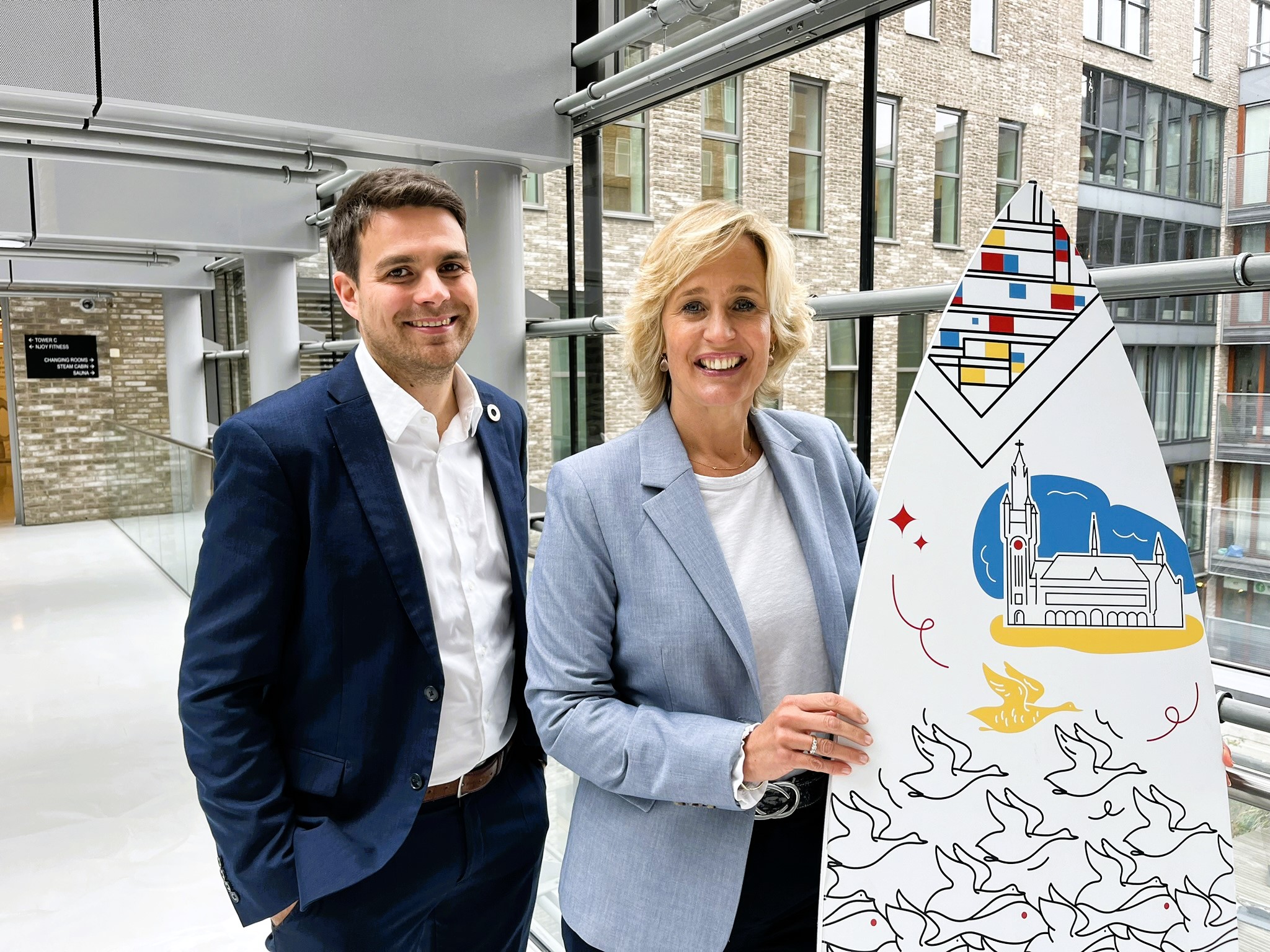 Image of international sales advisors Joris and Eline holding branded surfboard of The Hague in an urban area of The Hague