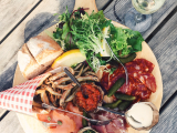 A wooden board with various snacks including meats, fish, and vegetables.