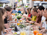 People sitting at a long table enjoying a meal outdoors.
