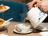A hand is pouring steaming tea into a cup.