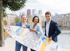Image of three people of The Hague and Partners holding a branded surfboard standing in front of the Hofvijver in The Hague