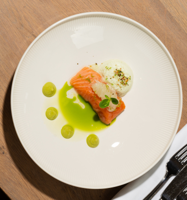 A plate with salmon, white sauce, and green drops.