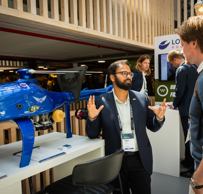 A man explaining something next to a blue drone at a fair.