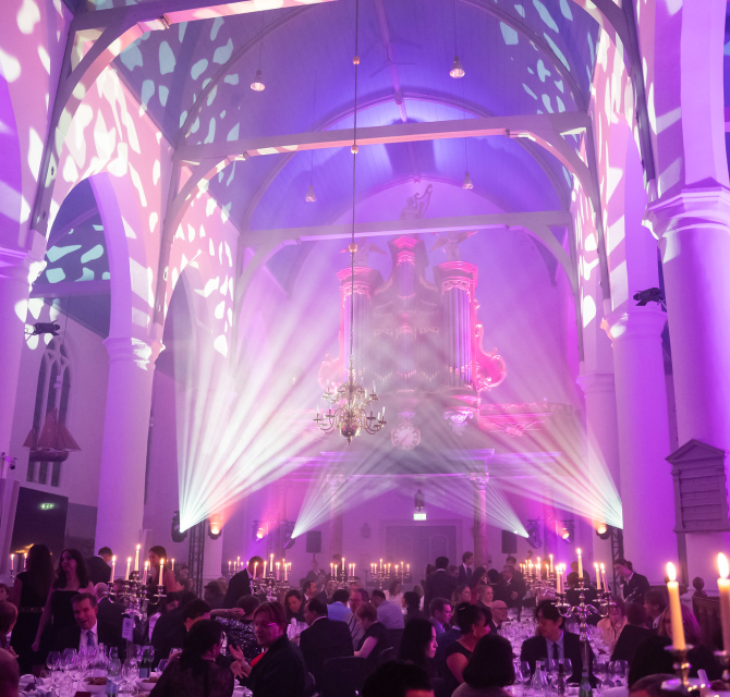 Interior of a hall with a light show and guests at dinner tables.