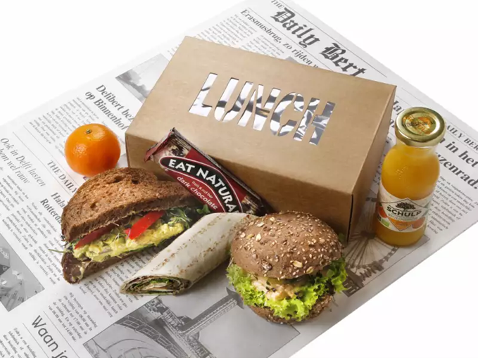 A lunchbox with sandwiches, an orange, an energy bar, and juice.