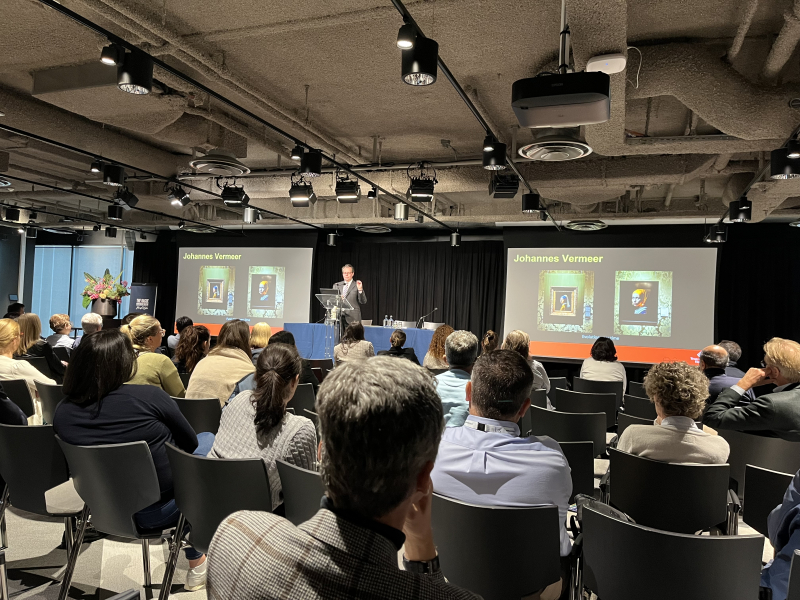 A speaker presents to an audience with images of Vermeer.
